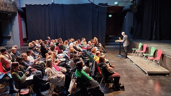 Bestuhlter Saal im Kulturzentrum Tollhaus mit Teilnehmenden, die sitzend einem Redner zum Runden Tisch Antirassismus / Antidiskriminierung am 27. Februar 2023 zuhören