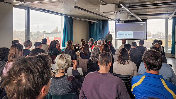 Redner der eine Präsentation vor einem Raum mit sitzenden Zuhörenden hält