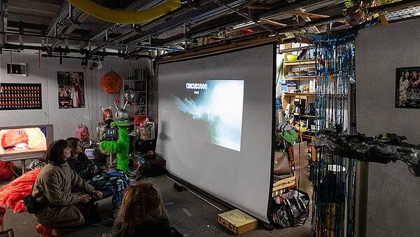 Drei Frauen vor einer Leinwand, die in einem Atelier einen Film schauen