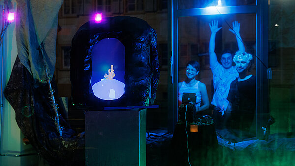 Ein bunt beleuchteter Bildschirm, auf dem eine Koralle zu sehen ist, mit drei Personen, die diesen durch ein Schaufenster betrachten