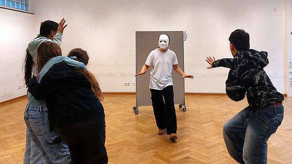 Aufnahme einer Probe, bei der ein Schüler mit Maske im Kreis seiner Mitschüler steht.