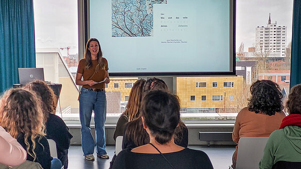 Rednerin vor einer Leinwand, die in einem Raum mit Zuhörerinnen spricht