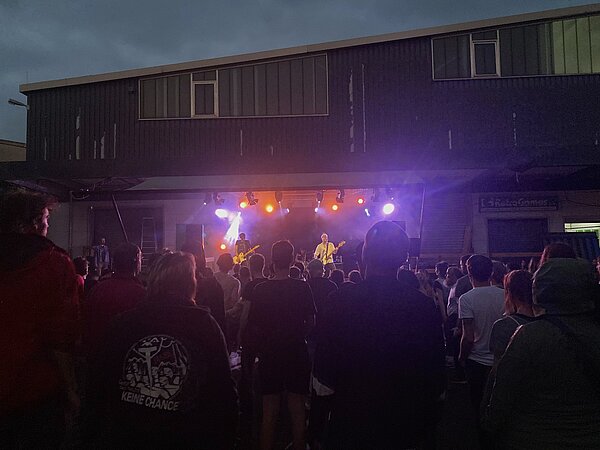 Blick auf eine Bühne vor dem Gebäude des p8, auf dem eine Band abends vor Publikum spielt