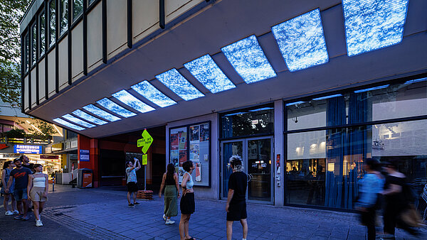 Personen vor einem Gebäude, die am Vordach angebrachte LED-Panels betrachten, die blau leuchten