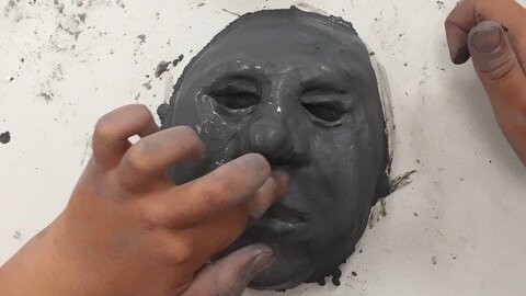 Kinderhände, die eine Gesicht aus Ton formen