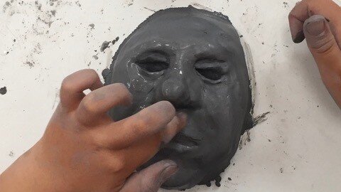 Kinderhände, die eine Gesicht aus Ton formen