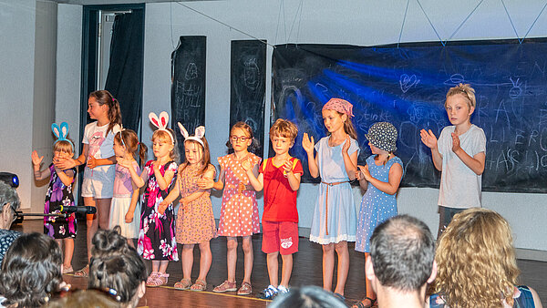 Kinder auf einer Bühne, in einer Reihe stehend und klatschend