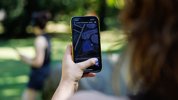 Nahaufnahme eines Smartphones in der Hand einer Person, auf der eine abstrahierte Karte zu sehen ist