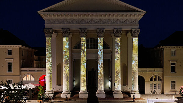 Großes klassizistisches Gebäude mit 6 hohen Säulen vor dem Eingang, auf die Rindenstrukturen projiziert werden