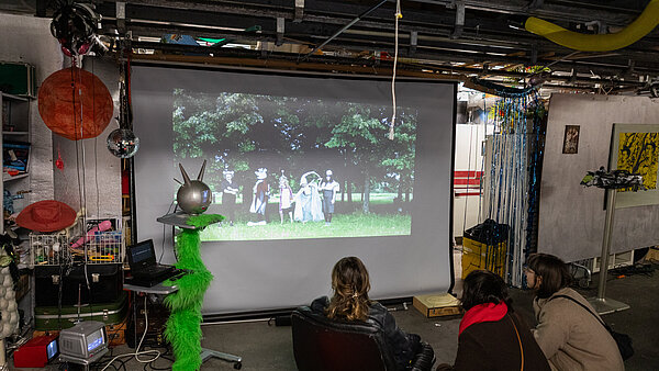 Drei Frauen vor einer Leinwand, die in einem Atelier einen Film schauen